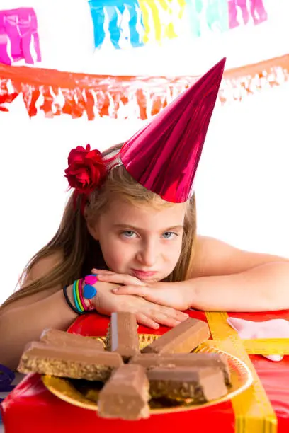 Bored gesture blond kid girl in party with chocolates and birthday hat