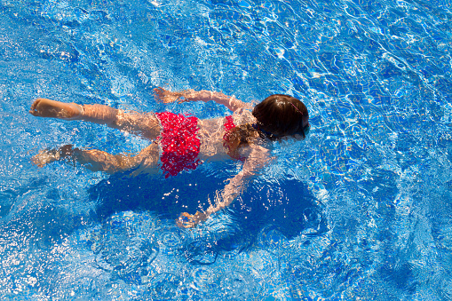bikini kid girl swimming on blue tiles pool in summer vacation