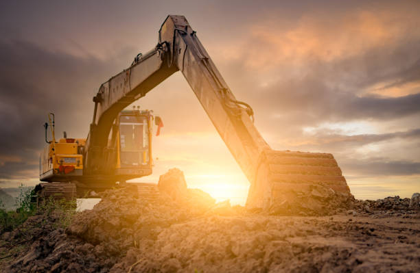 istock Backhoe parked at construction site after digging soil. Bulldozer on sunset sky and clouds background. Digger after work. Earth moving machine at construction site at dusk. Digger with dirt bucket. 1348367235