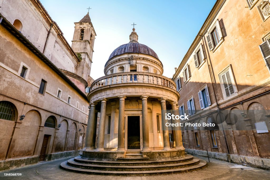 The Tempietto del Bramante in the courtyard of San Pietro in Montorio in Trastevere in the heart of Rome A suggestive perspective of the front side of the Tempietto in the courtyard of the church of San Pietro in Montorio, located on the Janiculum hill in the historic district of Trastevere, in the heart of Rome. Built in 1510 by the architect Donato Bramante, the Tempietto (Small Temple) is considered a masterpiece of Renaissance architecture, with the search for a perfect balance of shapes and volumes. The circular plan and the relationship between the dome and the colonnade recalls the classical values of Roman architecture, such as the famous Temple of Vesta located in the Roman Forum. According to tradition, the Tempietto was built to celebrate the martyrdom of St. Peter, which supposedly took place on the Janiculum. Trastevere is an iconic district of the Eternal City, due to the presence of countless artistic and historical treasures, monuments and ancient Romanesque and Baroque churches, but also for its squares and alleys to be explored freely, where it is easy to find typical restaurants, pubs, small shops of artisans and scenes of daily life with the original Roman soul. In 1980 the historic center of Rome was declared a World Heritage Site by Unesco. Super wide angle and high definition image. Rome - Italy Stock Photo