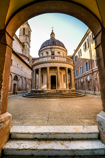 A suggestive perspective of the front side of the Tempietto in the courtyard of the church of San Pietro in Montorio, located on the Janiculum hill in the historic district of Trastevere, in the heart of Rome. Built in 1510 by the architect Donato Bramante, the Tempietto (Small Temple) is considered a masterpiece of Renaissance architecture, with the search for a perfect balance of shapes and volumes. The circular plan and the relationship between the dome and the colonnade recalls the classical values of Roman architecture, such as the famous Temple of Vesta located in the Roman Forum. According to tradition, the Tempietto was built to celebrate the martyrdom of St. Peter, which supposedly took place on the Janiculum. Trastevere is an iconic district of the Eternal City, due to the presence of countless artistic and historical treasures, monuments and ancient Romanesque and Baroque churches, but also for its squares and alleys to be explored freely, where it is easy to find typical restaurants, pubs, small shops of artisans and scenes of daily life with the original Roman soul. In 1980 the historic center of Rome was declared a World Heritage Site by Unesco. Super wide angle and high definition image.