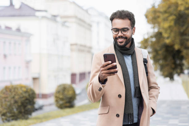 istock Handsome young man wearing warm clothing using smart phone in a city 1348369729