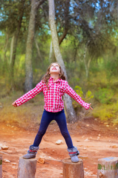 Side view of a young girl hiking at a park on a beautiful early autumn day. In this image she is on top of a granite hill, surrounded by trees.