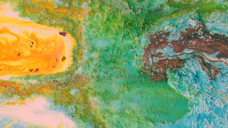 Fluid abstract acrylic and ink texture with colorful waves. Liquid paint and ink mixing. Red, yellow, green and metallic color.