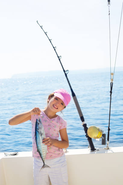 enfant petite fille pêchant dans un bateau tenant des petites prises de poisson tunny - descriptive color elementary student water blue photos et images de collection