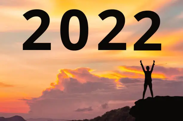 New Year 2022. Silhouette of winner person standing on the cliff. Sunset is on the background. Concept of changing the calendar year.