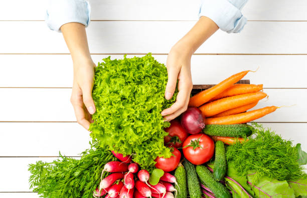 istock Woman’s hands holding wooden box with vegetables. Top view 1348372465