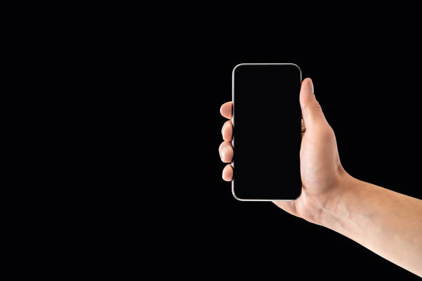 istock Phone and black background. Empty smartphone screen in dark. Mobile website design mockup. Hand holding cellphone to camera. Digital display with copy space. 1348373531