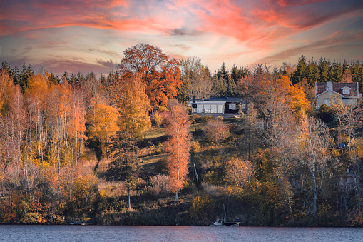 Cottage on a hill  in autumn colored forest. Beautiful sky on fire and lovely red, orange and yellow colored leaf