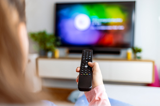 Shot of a young woman relaxing in front of her TV at the weekend