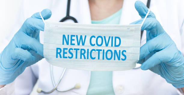 istock doctor's hands holding protective mask with text new covid restrictions 1348387357