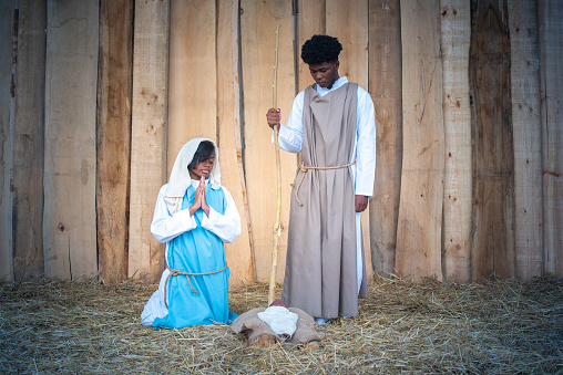 Nativity scene of a crib with african ethnic virgin mary and joseph praying and looking the jesus baby