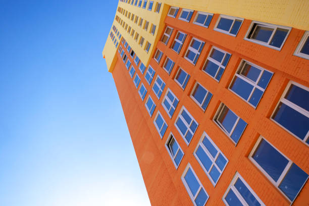istock Multi-colored modern residential high-rise building with many glass windows standing against background of blue sky and sun. Urban real estate stock photo 1348390592