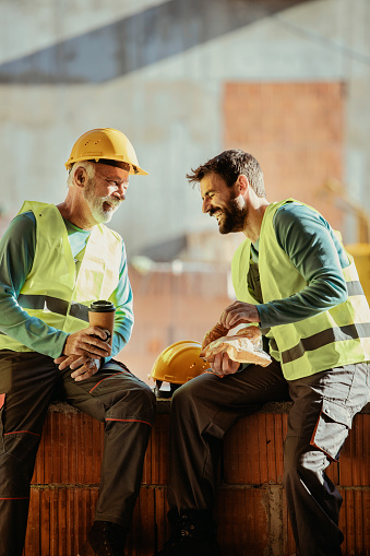 Construction Workers on a Break at a Building Site Sitting on the Stone Surface Against the Construction Site