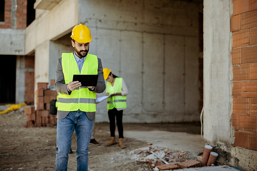 Construction Manager Using Tablet on Building Site Outdoors in Front of His Colleagues. Building Site Place on Background. Construction Concept