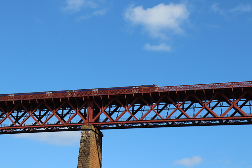 Looking up at train on old railway bridge against blue sky with fluffy white cloud