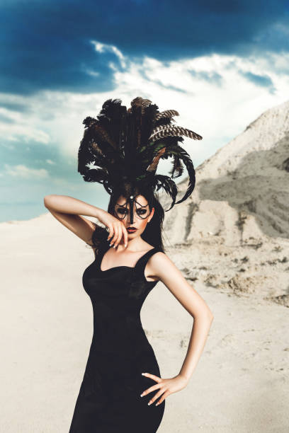 attractive model in a black dress against a background of white sand. girl with a feather ornament on her head. concept is beauty and fashion. attractive model in a black dress against a background of white sand. girl with a feather ornament on her head. ostrich feather stock pictures, royalty-free photos & images