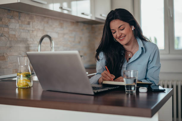 istock Businesswoman using a laptop while working in the kitchen at home 1348414938