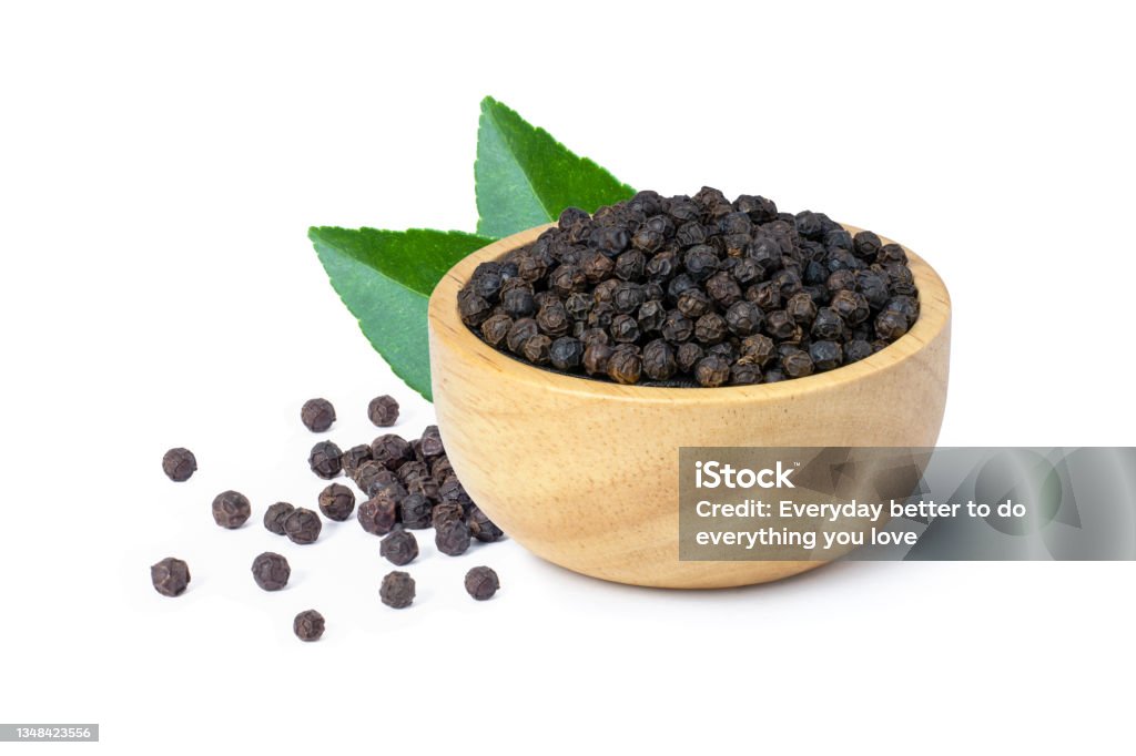 Black pepper (peppercorn) isolated on white Black pepper seeds or peppercorns (dried seeds of piper nigrum) in wooden bowl with green leaf isolated on white background. Black Peppercorn Stock Photo