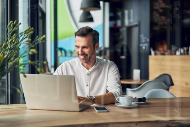 istock Smiling businessman working on laptop in cafe 1348456125