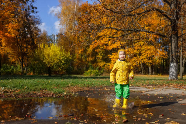 istock smiling child boy in yellow raincoat have fun with puddle 1348456661