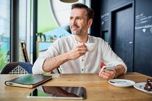 Handsome man drinking coffee in cafe using smartphone