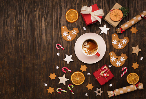 Gingerbread cookies with cup of coffee, Christmas and New Year decor, gift boxes, candy canes, cinnamons on dark wooden background. Concept of holiday winter food.