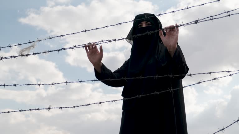 Refugee woman  standing behind a fence