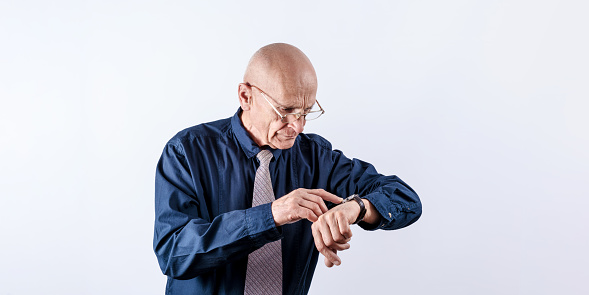 Photography of hairless elder businessman in glasses looking at wristwatch. Punctuality and meeting concept.