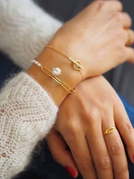 Gold bracelets accumulation and ring on a woman wrist wearing a white wool winter pullover stock photo