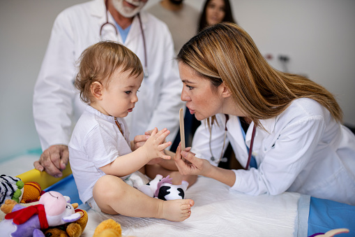 Female pediatrician playing with baby boy on the table in doctors