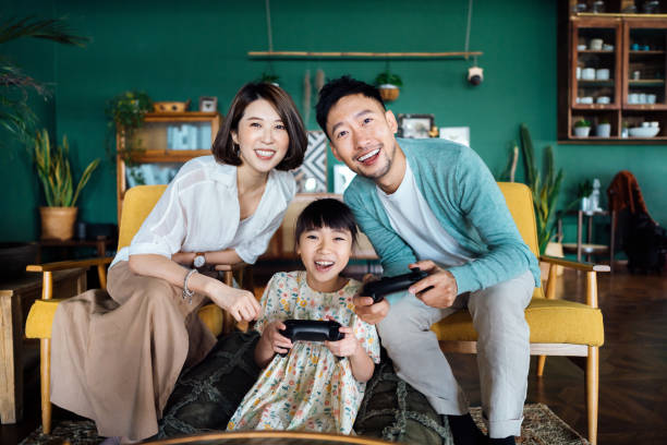 giovane famiglia asiatica felice e figlia che trascorrono un po 'di tempo insieme, divertendosi a giocare ai videogiochi mentre si siedono sul divano nel soggiorno di casa - video game family child playful foto e immagini stock