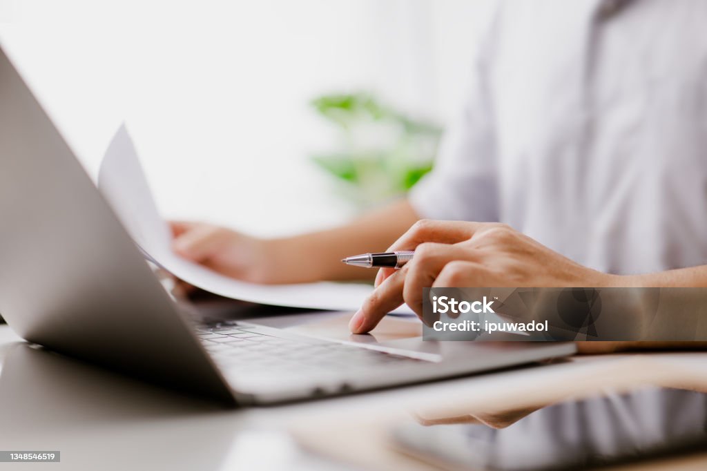 Businessman hand is on the trackpad, typing on a laptop keyboard, while reading a business document. In a modern office, a corporate man, a lawyer, works. Concept of business and technology. Document Stock Photo
