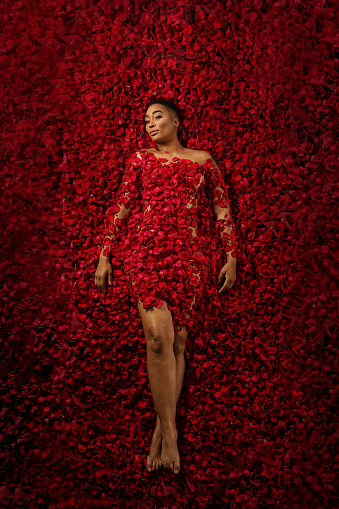 A beautiful woman laying in a colourful bed of red roses and other flowers