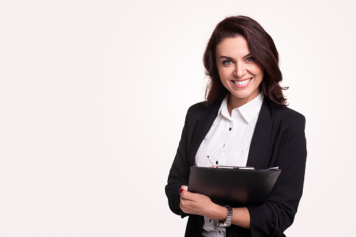 Confident smiling business lady in black formal suit and white shirt holding clipboard with documents and looking at camera on white background with blank space