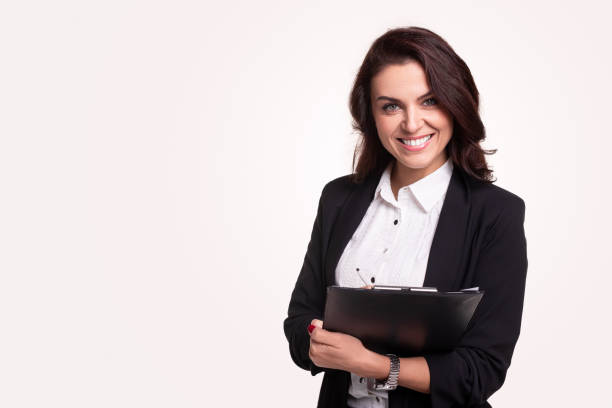 Smiling businesswoman with clipboard looking at camera Confident smiling business lady in black formal suit and white shirt holding clipboard with documents and looking at camera on white background with blank space advice photos stock pictures, royalty-free photos & images