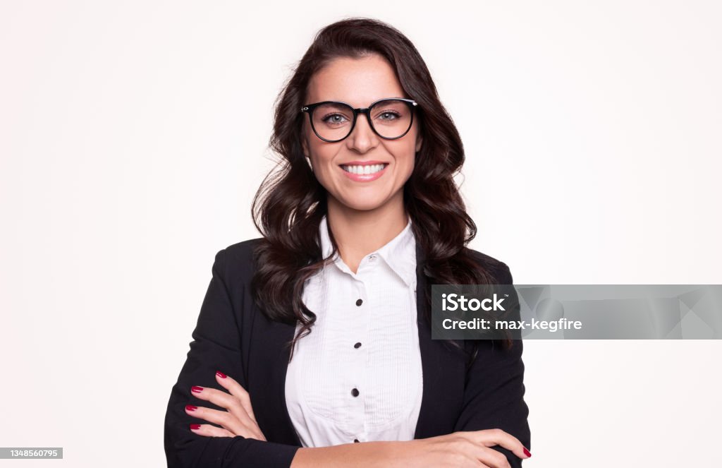 Confident business lady in eyeglasses smiling at camera Happy successful adult businesswoman in formal outfit and stylish glasses smiling and looking at camera while standing with arms crossed against white background White Background Stock Photo