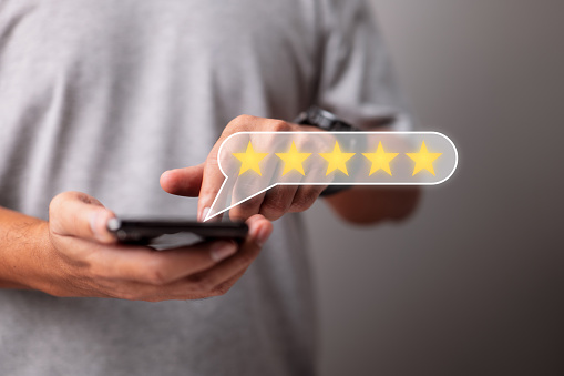 Man hand holds a smartphone with a five-star icon for customer service experience, feedback evaluation, and business satisfaction survey.