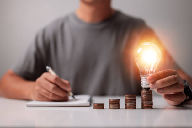 istock Businessman holds a light bulb while stacking coins on his desk. The concept of saving energy and money. 1348565931