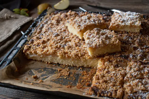 Traditional german rustic apple crumble cake. Fresh baked and still warm. Served on a baking tray on wooden table background. Closeup view from above