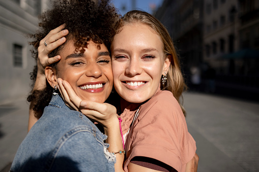 Portrait of a young diverse group of female friends meeting and greeting each other in the city, hugging and having fun together outdoors, smiling and expressing love to one another