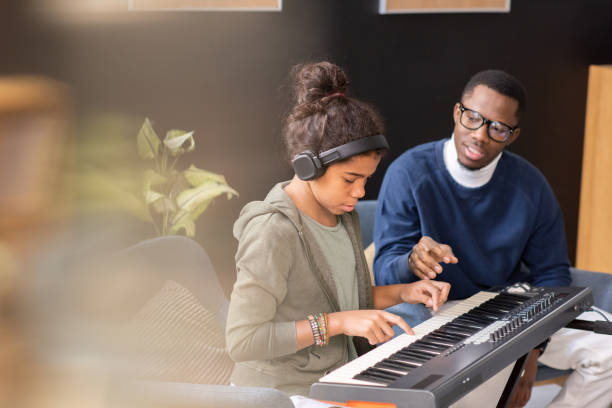 Cute schoolgirl pushing keys of piano keyboard during home lesson Cute diligent schoolgirl pushing keys of piano keyboard while teacher helping her during home lesson juvenile musician stock pictures, royalty-free photos & images