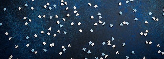 White and blue small stars of sweets on a dark blue concrete or stone background. Selective focus. Christmas composition. Top view. Copy space.