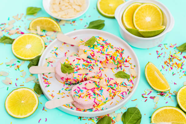 Bright and colorful flat lay of pink strawberry Popsicle ice cream with sliced lime and mint on blue background. Healthy summer food concept. Top view of popsicle with sprinkles, overhead