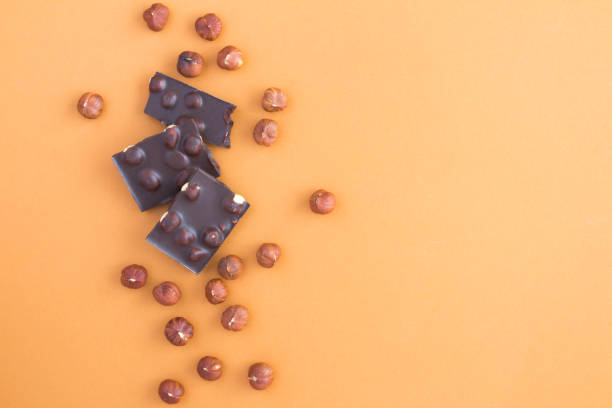 istock Pieces of dark chocolate with hazelnuts on the light brown background. Top view. Copy space. 1348584271