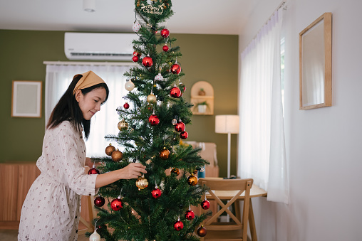 Women preparing and hanging decorations on christmas tree at home.