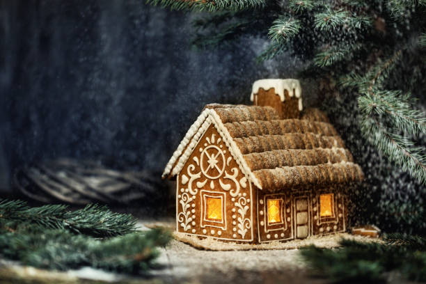 夜の冬の雪の森の窓ライトとクリスマスジンジャーブレッドハウス。コピースペースと暗い背景の上にクリスマスホリデーのための創造的な食品装飾デザイン