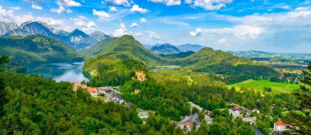 Panoramic view of Hohenschwangau Castle in the Allgäu in the middle of the alpine landscape with lakes seen from a public vantage point