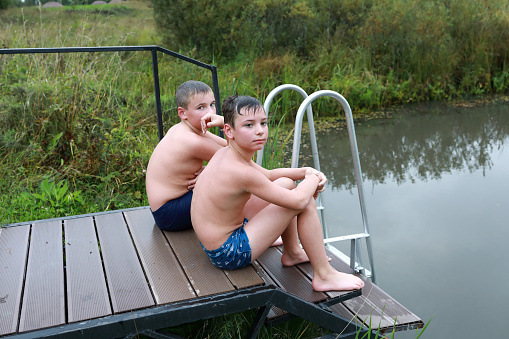 Kids sitting on wooden bridge by pond, Karelia