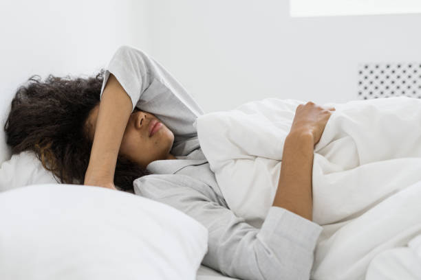 Sad african american woman covered face with hand Side view of sad african american woman covered face with hand. Tired dark skinned female lying on bed in pajamas, spending early morning at home, sleeping after stressful night person waking up stock pictures, royalty-free photos & images